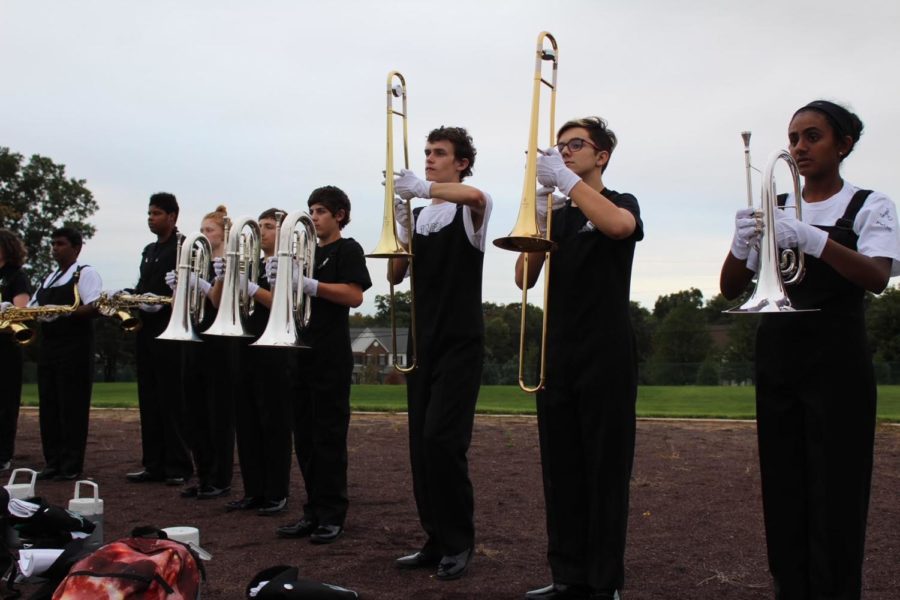 The mellophones, trombones, baritones and tenor saxophones stand at set waiting for the drum major to begin conducting. 
