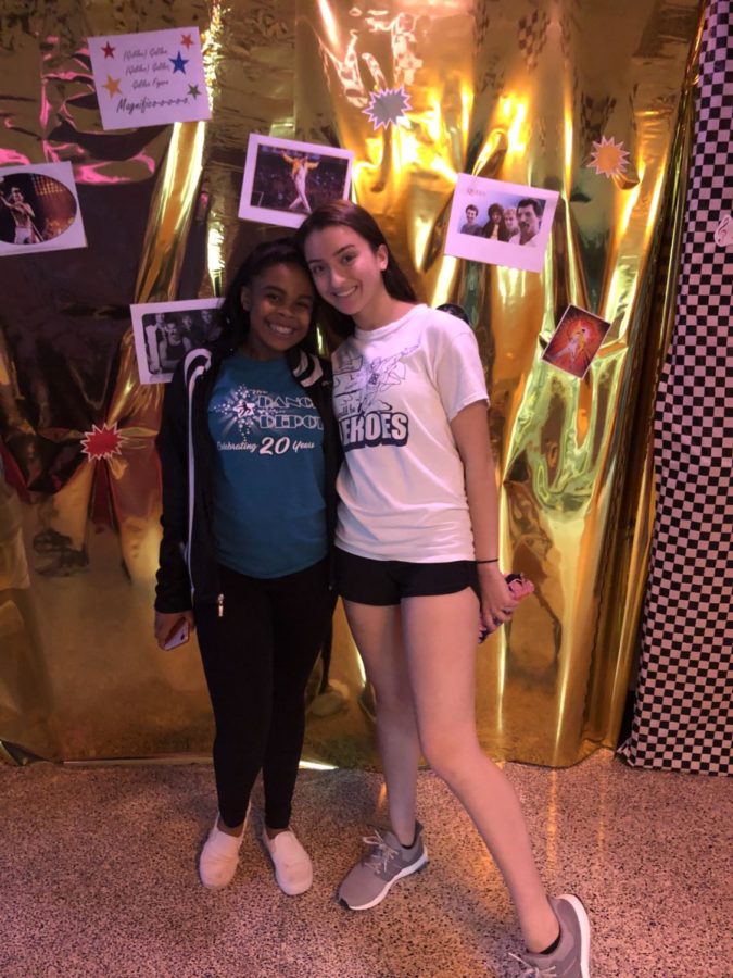 Sarah Hunsicker and Siani Ford-Barkley stand together in front of a wall dedicated to Queen. 
