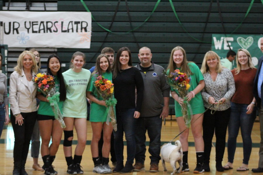 All three seniors pose on the volleyball court for a photo with their friends and family.
