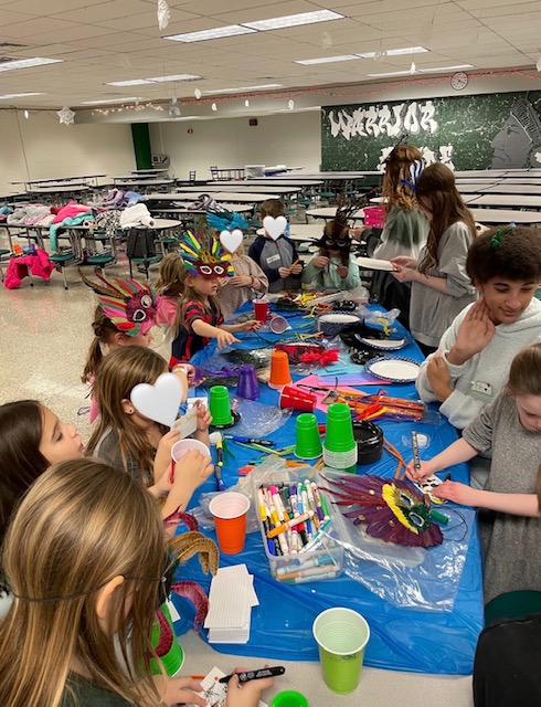 The props table is covered in masks, markers, and cups. The students can be seen unleashing their creativity and eagerly unlocking endless crafty opportunities. 