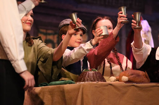 Tiny Tim (Alex Zawadzki) cheers with his fellow Cratchit family members Belinda (Caroline Fitzgerald) and Martha (Kira Sands)
